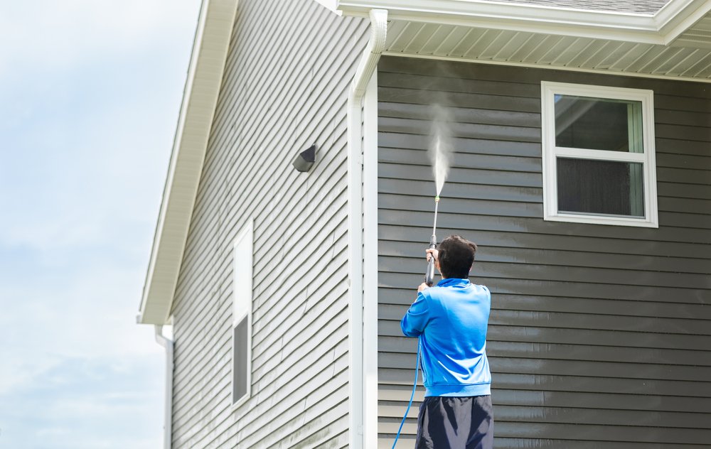 a man wearing blue pressure washing his house